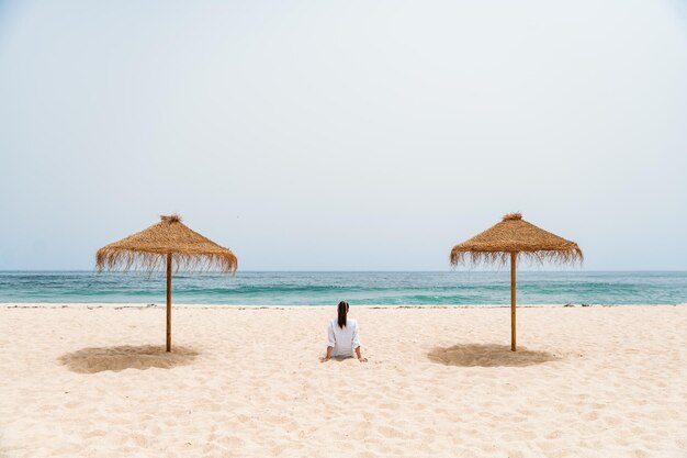 Viaggiatore femminile che si siede sulla sabbia vicino all'oceano