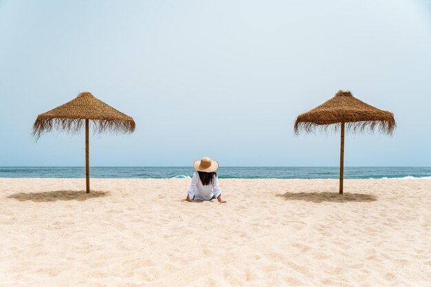 Viaggiatore femminile che si siede sulla sabbia vicino all'oceano