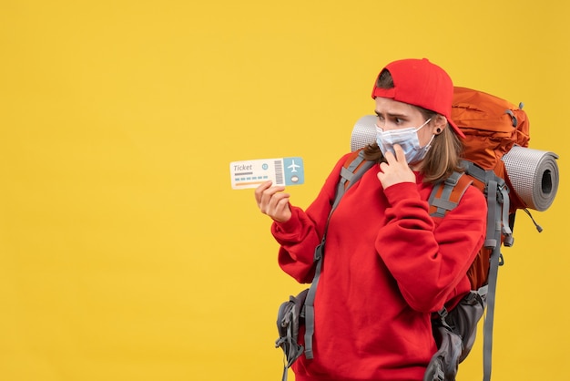 Viaggiatore femminile confuso vista frontale con zaino e maschera che tiene biglietto aereo