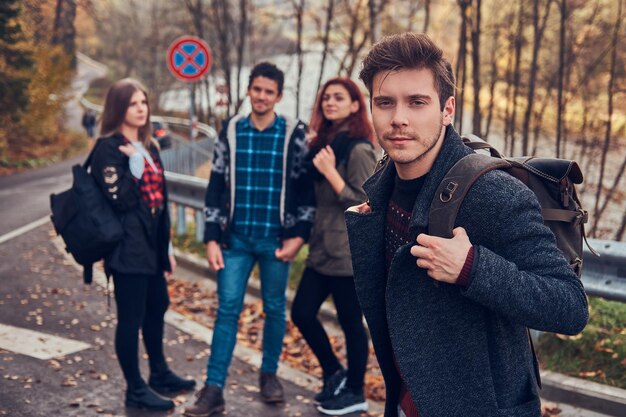 Viaggio, autostop, concetto di avventura. Gruppo di giovani escursionisti in piedi ai margini della strada nella bellissima foresta autunnale.