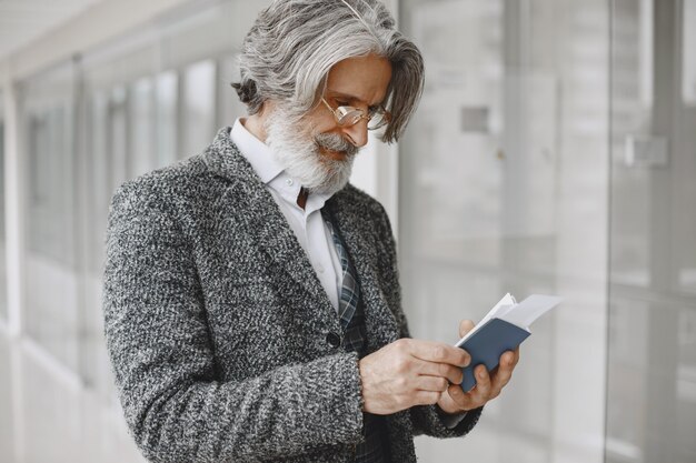 Viaggio di lavoro. Concetto aziendale e di persone. Maschio con mantello grigio. Senior con un passaporto.