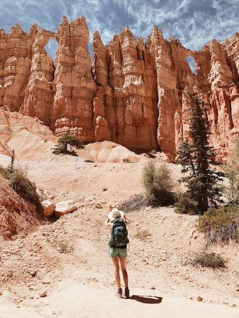 Viandante femminile in pantaloncini e un cappellino da sole in piedi di fronte a grandi formazioni rocciose e scogliere