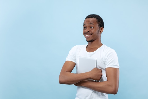 vicino ritratto di giovane uomo afro-americano in camicia bianca. Emozioni umane, espressione facciale, annuncio, concetto di vendita. Tenendo una tavoletta e sorridendo. Sembra felice.