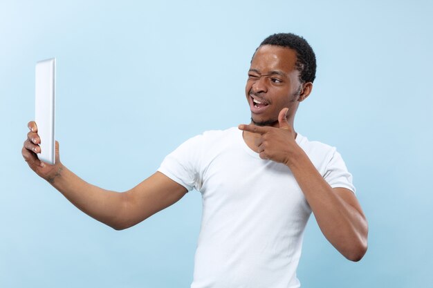 vicino ritratto di giovane uomo afro-americano in camicia bianca. Utilizzo di tablet per selfie, vlog, parlare.