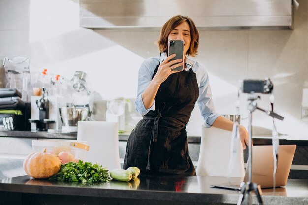 Videoblogger della giovane donna che cucina alla cucina e alle riprese