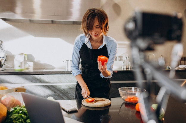 Videoblogger della giovane donna che cucina alla cucina e alle riprese