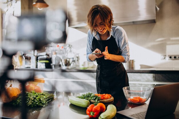 Videoblogger della giovane donna che cucina alla cucina e alle riprese