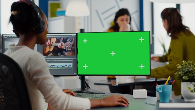 Videografo nero che utilizza computer con chroma key mock up display isolato editing video e audio f...