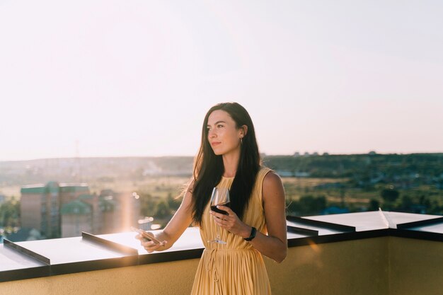 Vino bevente della bella donna sul tetto alla luce solare