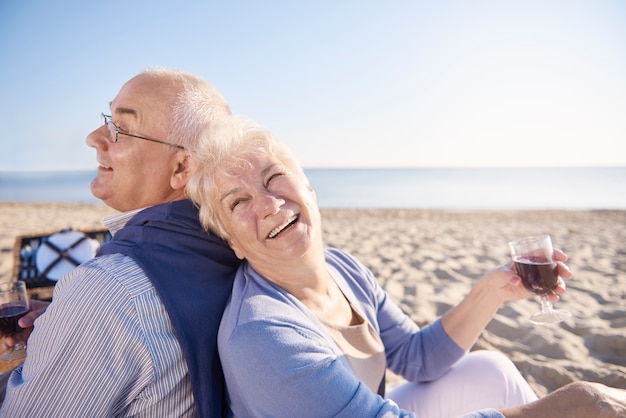 Vino rosso bevuto in spiaggia. Coppia senior in spiaggia, il pensionamento e il concetto di vacanze estive