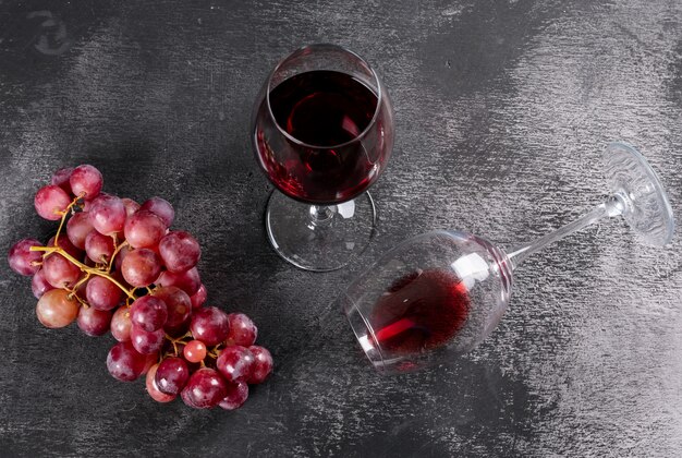 Vino rosso di vista laterale con l'uva sull'orizzontale di pietra nero