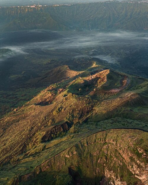 Vista a volo d'uccello di colline ricoperte di vegetazione e nebbia sotto la luce del sole: perfetta per le carte da parati