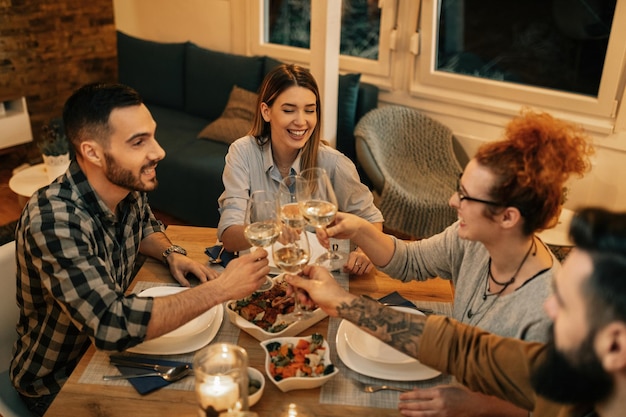 Vista ad alto angolo di amici felici che brindano con il vino mentre cenano insieme