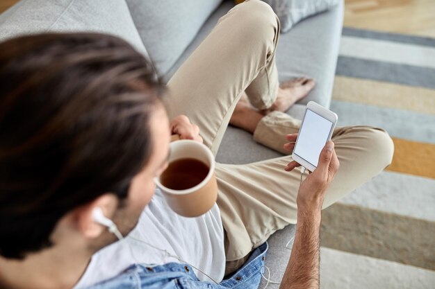 Vista ad alto angolo di un uomo che beve caffè e usa lo smartphone mentre ci si rilassa sul divano Spazio di copia