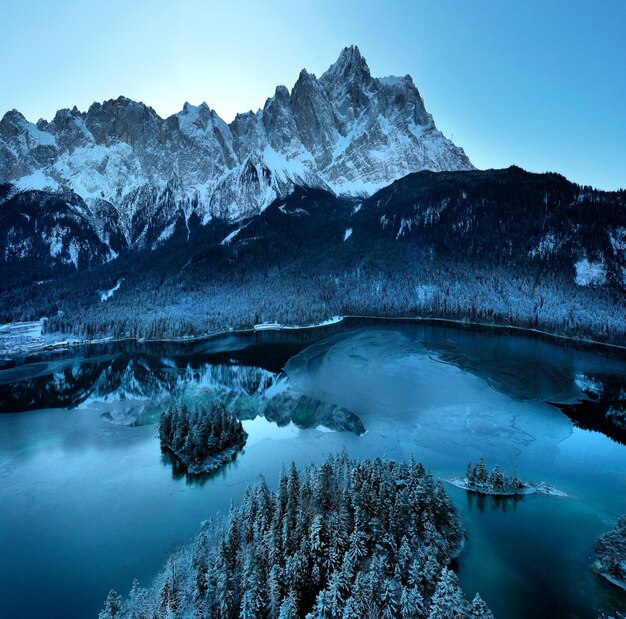 Vista aerea del fiume Eibsee ghiacciato circondato da alberi coperti di neve in Baviera, Germania