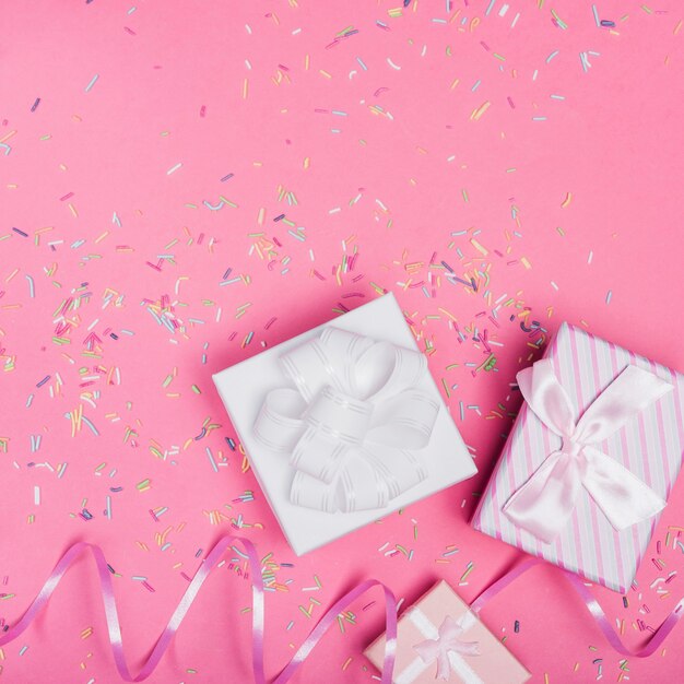 Vista aerea di scatole regalo con nastro arricciatura e cospargere su sfondo rosa