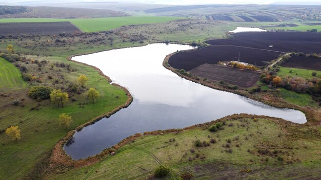 Vista aerea drone della natura in Moldova, lago con cielo nuvoloso che riflette, campi seminati, alberi