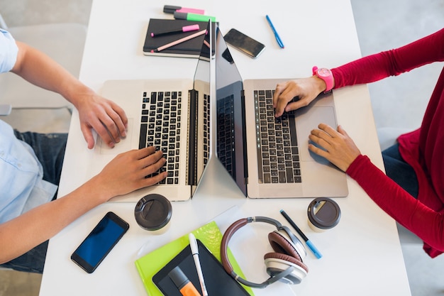 Vista da avove sulle mani di giovane uomo e donna che lavora al computer portatile in ufficio di co-working