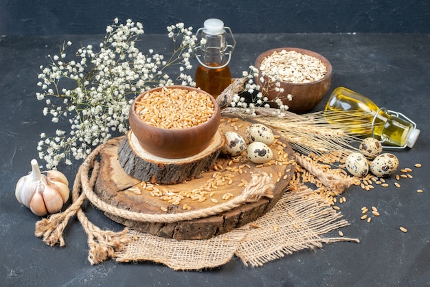 Vista dal basso chicchi di grano in una ciotola aglio su tavola di legno naturale uova di quaglia bottiglia di olio avena ciotola fiori di gypsophila sul tavolo