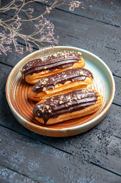 Vista dal basso eclairs al cioccolato sul piatto ovale ramo di fiori secchi sullo sfondo di legno scuro