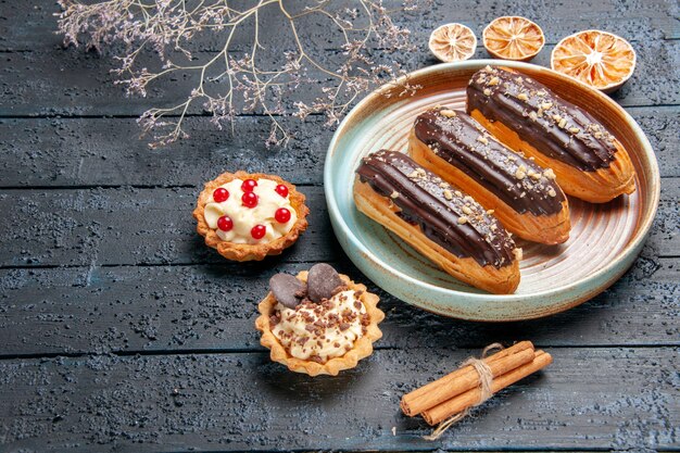 Vista dal basso eclairs al cioccolato sulla piastra ovale fiore essiccato crostate di ramo cannella e arance essiccate sul tavolo di legno scuro con spazio di copia