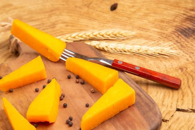 Vista dal basso fette di formaggio pepe nero e forchetta su tagliere pane a spiga di grano su superficie di legno