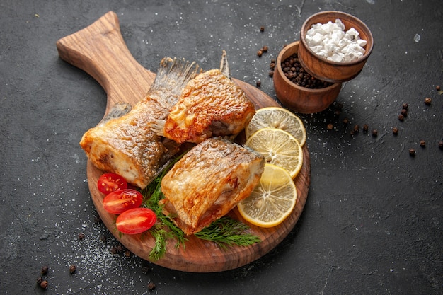 Vista dal basso frittura di pesce fette di limone tagliate pomodorini sul tagliere spezie diverse in ciotole su sfondo nero