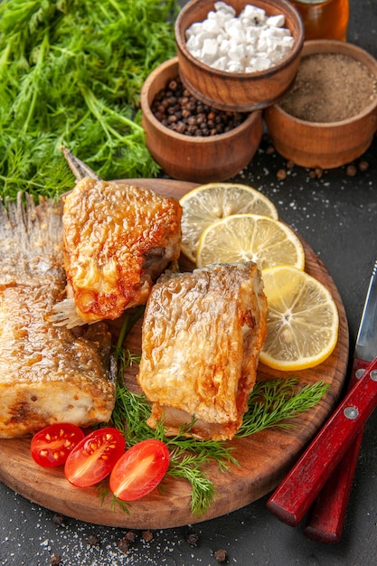 Vista dal basso gustosa frittura di pesce fette di limone tagliate pomodorini sul tagliere spezie diverse in ciotole su sfondo nero