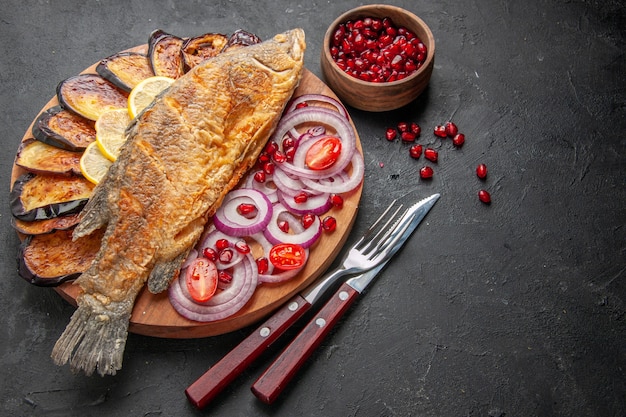 Vista dal basso, gustose fritture di pesce, melanzane fritte, cipolle tagliate su tavola di legno e altri alimenti su sfondo scuro