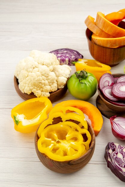 Vista dal basso le verdure fresche hanno tagliato le cipolle il pomodoro verde ha tagliato il cavolo rosso i peperoni gialli il cavolfiore in ciotole sul tavolo di legno bianco