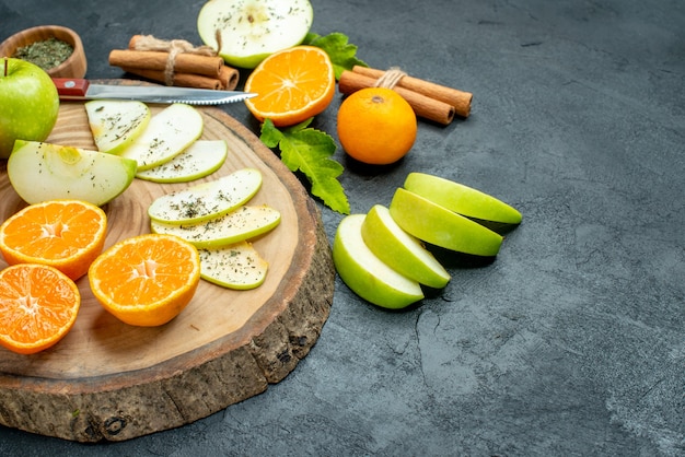 Vista dal basso mela e mandarini fette coltello su tavola di legno bastoncini di cannella legati con corda polvere di menta essiccata in una ciotola sulla tavola nera