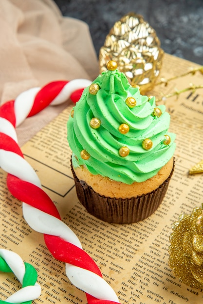 Vista dal basso mini cupcake natale caramelle ornamenti natalizi su giornale beige tule scialle su sfondo scuro