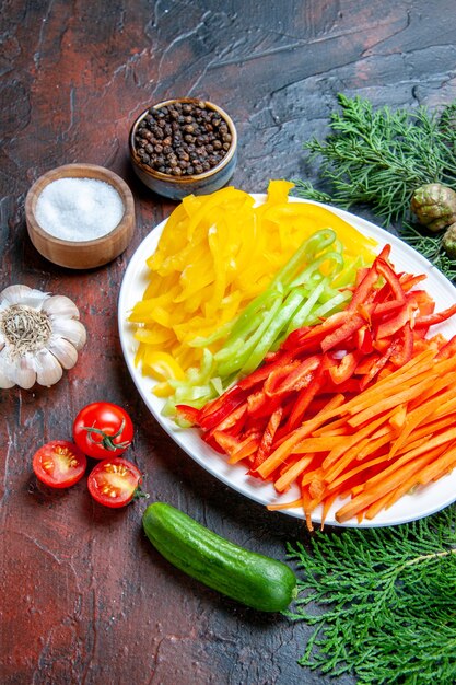 Vista dal basso peperoni tagliati colorati su piatto sale e pepe nero pomodori aglio cetriolo sul tavolo rosso scuro