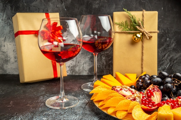 Vista dal basso pezzi di formaggio carne uva e melograno su tavola ovale bicchiere di vino regali di natale al buio