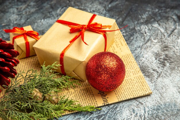 Vista dal basso piccoli regali legati con nastro rosso palla di Natale ramo di pino su giornale su sfondo scuro