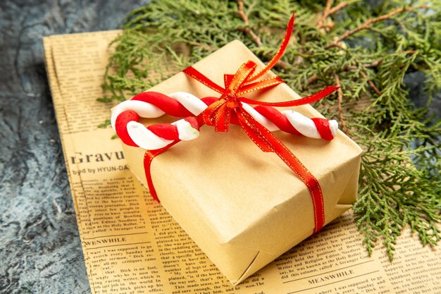 Vista dal basso piccolo regalo legato con nastro rosso caramelle natalizie su giornale su grigio