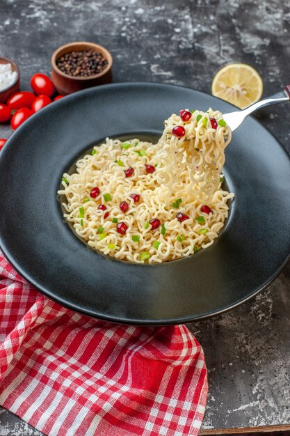 Vista dal basso ramen noodles sollevati su una forchetta su piastra nera pepe nero in una ciotola pomodorini tagliati al limone sul tavolo scuro