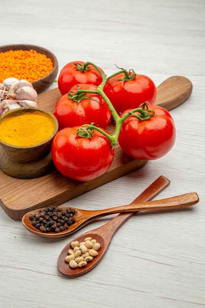 Vista dal basso ramo di pomodoro fresco aglio curcuma su tagliere cucchiai di legno con pepe nero e fagioli su tavola grigia