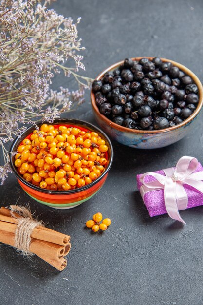 Vista dal basso ribes nero olivello spinoso in ciotole piccoli bastoncini di cannella regalo su superficie scura dark