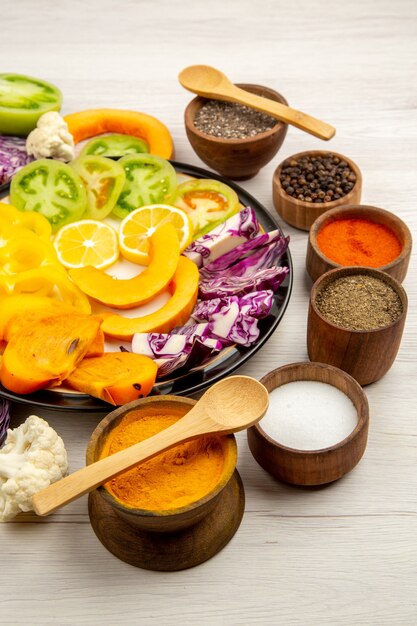 Vista dal basso tagliare frutta e verdura zucca peperoni persimmon cavolo rosso sulla piastra nera spezia in piccole ciotole cucchiaio di legno sul tavolo di legno