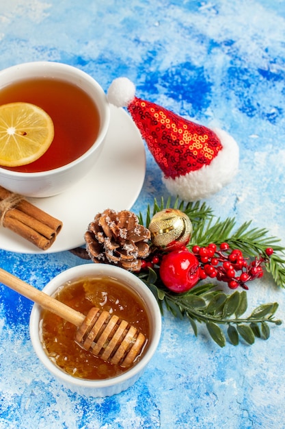 Vista dal basso tazza di tè al miele in una ciotola con cappello di Babbo Natale con bastoncino di miele sul tavolo blu