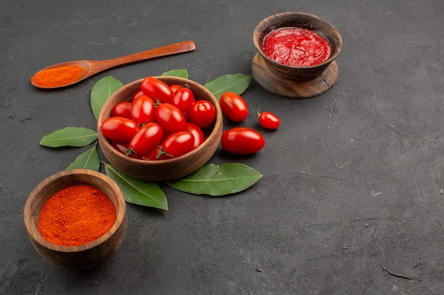 Vista dal basso una ciotola di pomodorini foglie di alloro un cucchiaio di legno e ciotole di ketchup e peperoncino in polvere sulla tavola nera