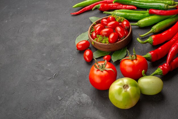 Vista dal basso una ciotola di pomodorini peperoni rossi e verdi caldi e pomodori e foglie di alloro su sfondo nero