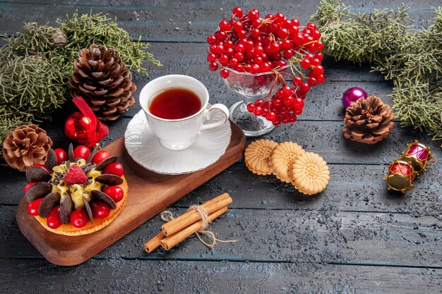 Vista dal basso una tazza di tè e torta di frutti di bosco sul piatto da portata di legno ribes in un vetro pigne nelle quali giocattoli di natale foglie di abete sul tavolo di legno scuro