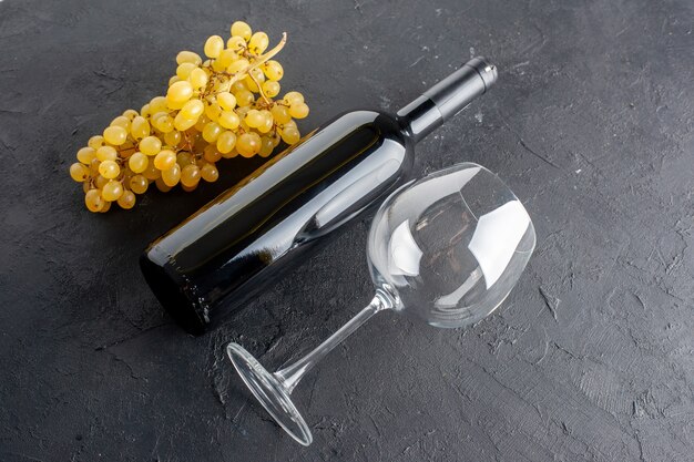 Vista dal basso uva gialla fresca bottiglia di vino e apribottiglie in vetro sul tavolo scuro