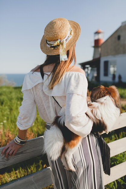 Vista dal retro di una donna elegante in campagna, con in mano un cane