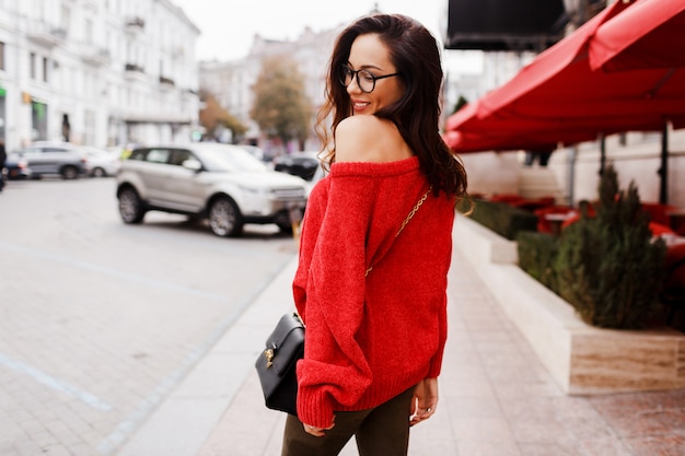 Vista dal retro. Immagine di moda di strada di bella donna mora in maglione rosso alla moda, abito primaverile walk-in per la strada.