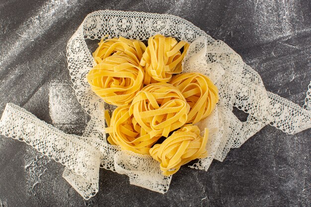 Vista dall'alto a forma di pasta italiana a forma di fiore crudo e giallo sulla scrivania grigia spaghetti crudi italiani