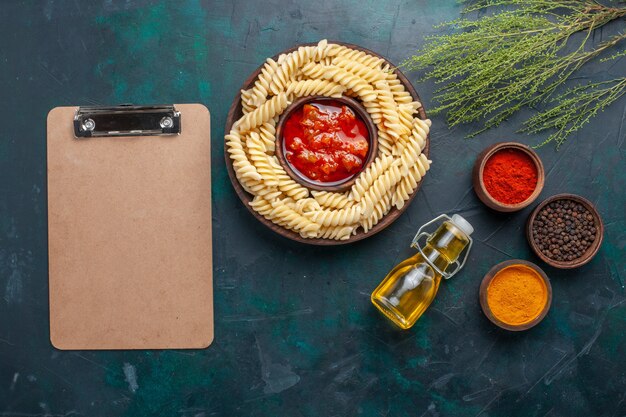 Vista dall'alto a forma di pasta italiana con olio e condimenti diversi su sfondo blu scuro