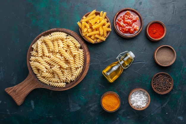 Vista dall'alto a forma di pasta italiana con salsa e condimenti sulla scrivania blu scuro